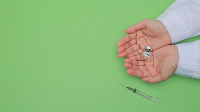 Scientist hand holding peptide vial for research beside syringe shows dedicated care in green laboratory setting for clinical health treatment