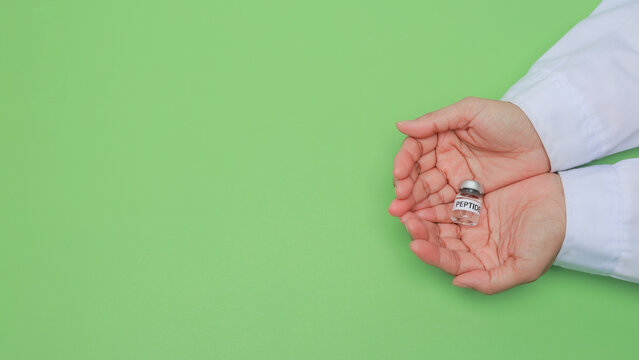 Careful scientist hand gently holding peptide vial for healthcare medical research with hopeful care against plain green background