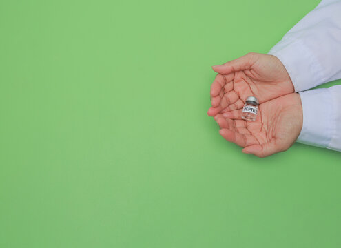 Dedicated scientist hand holding medical peptide vial with careful hope during laboratory research over green background