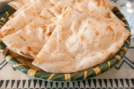 Fresh baked Indian naan flatbread slices served on a woven plate.