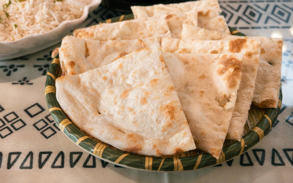 Fresh baked Indian naan flatbread slices served on a woven plate.