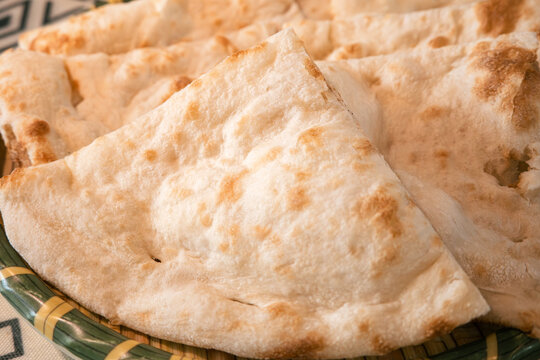 Fresh baked Indian naan flatbread slices served on a woven plate.