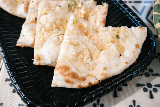 Fresh baked Indian naan flatbread slices served on a woven plate.