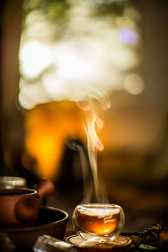 View of steaming tea in a glass cup with a ceramic teapot in the background, warm lighting, soft bokeh in Ashland, OR, United States.
