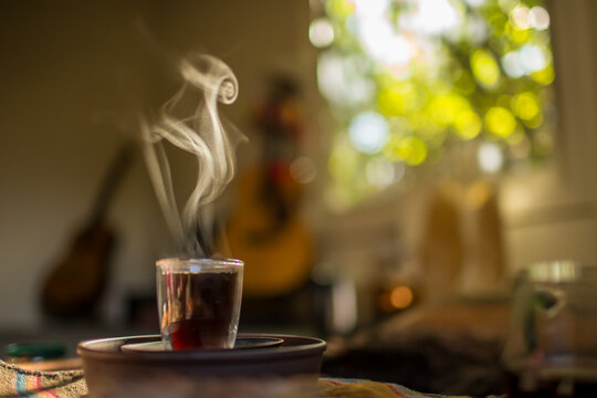 View of a steaming glass of tea on a dark saucer with a blurred background featuring a guitar and soft natural light in Ashland, OR, United States.