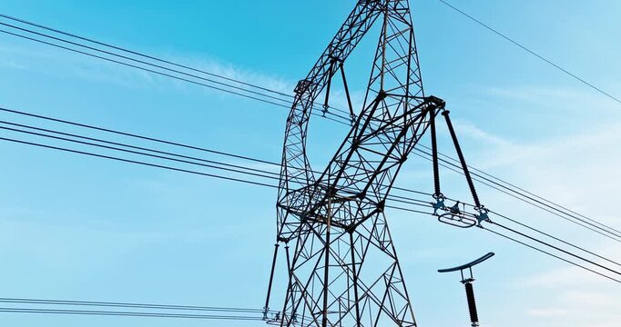 A steel high-voltage transmission pylon stands against a clear blue sky, showing complex lattice steel framing and connected power cables under bright sunlight.