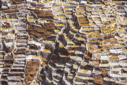 View of the Salt Mine of Maras featuring intricate terraced evaporation ponds with varying shades of white and brown earth in Urubamba, Cusco, Peru.