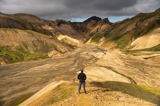 View of a hiker standing on a ridge overlooking the colorful volcanic mountains and braided river valley of Landmannalaugar, Rangarthing ytra, Iceland.