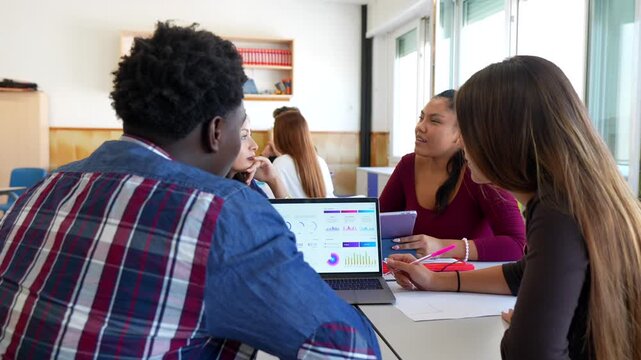 Multiracial group of young university students studying and analyzing data charts on a computer screen in a classroom, showcasing teamwork and collaborative learning in higher education