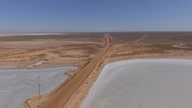 Aerial view of the vast Aral salt flats with a long dirt road stretching through the arid desert landscape under a clear blue sky in Aral, Kyzylorda Region, Kazakhstan.