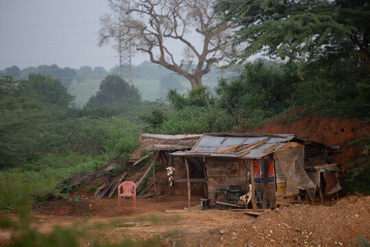 View of a rustic makeshift shelter with a motorcycle and a red plastic chair surrounded by lush vegetation in Dikwella, Southern Province, Sri Lanka.