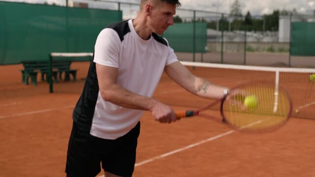 Caucasian young adult man bouncing tennis ball and performing powerful serve on clay court in slow motion. Clip suits sports training campaigns and athletic fitness promotions
