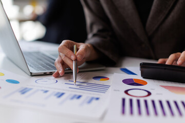 Business professional analyzing financial data and statistics using a calculator and laptop,...