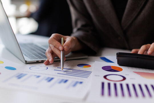 Business professional analyzing financial data and statistics using a calculator and laptop, working on budget reports and market analysis with charts and graphs