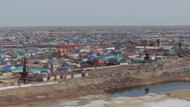 Aerial view of Aral town with industrial cranes and a mosque featuring golden domes set against a dry landscape in Aral, Kyzylorda Region, Kazakhstan.