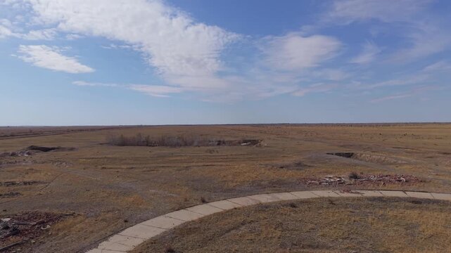 Aerial view of the vast arid landscape of the Semipalatinsk Nuclear Test Site with a winding dirt road under a clear blue sky in Semey, Abai Region, Kazakhstan.