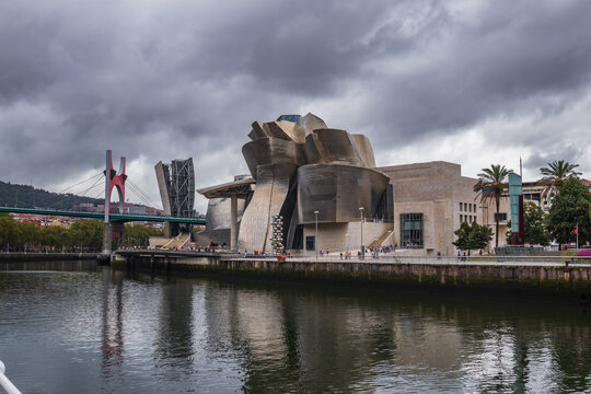 Bilbao, Pais Vasco, Espa&ntilde;a. 1 de Serptiembre 2026. Arquitectura vanguardista del Museo Guggenheim junto a la r&iacute;a del Nervi&oacute;n y el puente La Salve, bajo un dram&aacute;tico cielo cubierto de nubes.