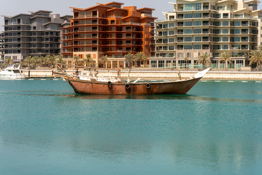 View of a traditional pearl-diving dhow floating in the calm harbor waters with modern residential buildings in the background in Manama, Capital Governorate, Bahrain.