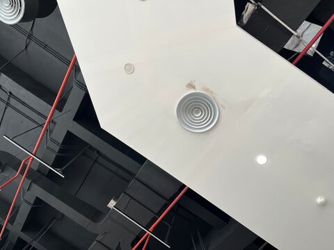 Modern industrial ceiling with circular air vents and red utility pipes in a large building.