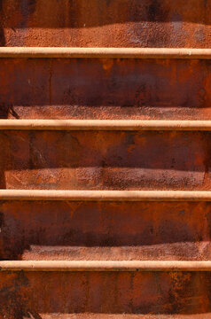 Heavily rusted red metal surface with horizontal bars and shadows, grunge industrial texture background.