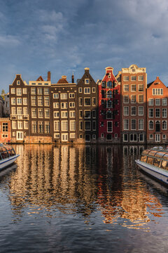 View of the historic gabled canal houses along the Damrak reflecting in the calm water with canal boats under a clear blue sky in Amsterdam, Noord-Holland, Netherlands.