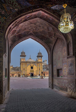 View of Wazir Khan Mosque framed by an ornate archway with intricate tile work and a hanging chandelier in the courtyard, Lahore, Punjab, Pakistan.
