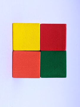 wooden toy blocks. A top-down view of four colorful wooden building blocks arranged in a square shape on a plain white surface.