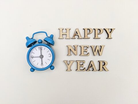 Wooden letters spell out Happy New Year beside a blue alarm clock, creating a festive, hopeful mood. Ideal for holiday, celebration, timing and new beginnings themes