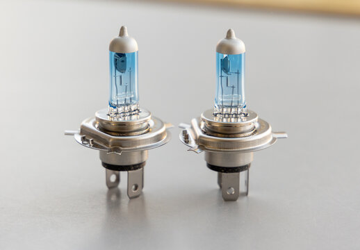 Two H4 Halogen Car Headlight Bulbs with Blue Tint on Gray Background