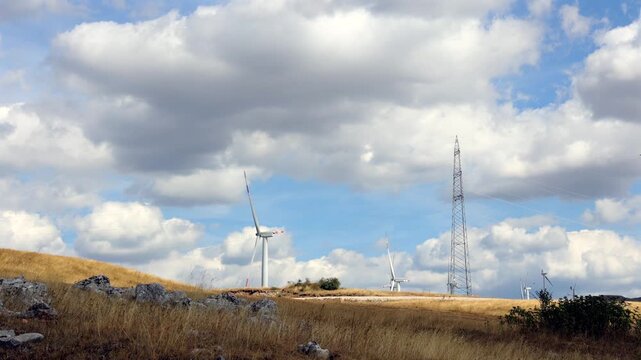 Wind Turbines and Power Line Under Moving Clouds Timelapse. Timelapse of wind turbines and power line on dry hills under moving clouds in a renewable energy landscape.