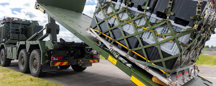 Military hook-lift truck unloads cargo pallet secured netting loading ramp airfield. Airforce logistics operation transport, deployment readiness, mobility support and defense infrastructure
