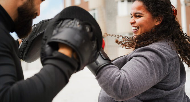 Curvy african american girl and her personal trainer doing boxing sport outdoor - Sport, diet and healthy lifestyle concept - Main focus on woman face - UGC content