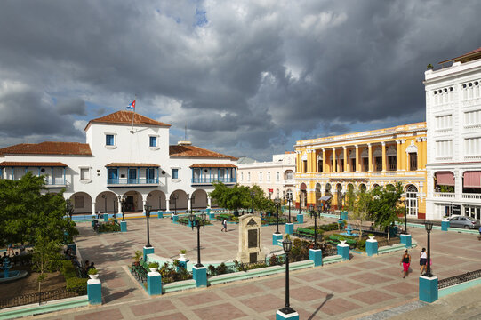 View of Parque Cespedes with its historic colonial architecture, paved square, and people walking under a cloudy sky in Santiago de Cuba, Santiago de Cuba, Cuba.