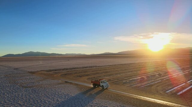 White salt flat patterns, a lone mining truck and long extraction rows sit under a low sunrise in Salinas Grandes, Argentina, with the camera orbiting slowly.