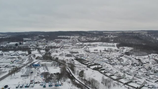 Aerial drone view overlooking snow covered Angered with residential buildings, roads, wooded areas and rolling hills stretching across the winter landscape from Storas, Gothenburg, Sweden