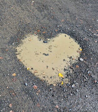 Heart shaped puddle on gravel road close-up, muddy water with autumn leaves concept