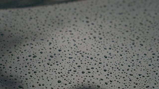 Macro close up of tiny raindrops resting on a glossy black metallic surface, creating detailed water patterns, reflections and an abstract automotive texture.