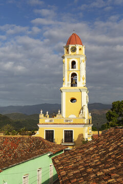 View of the iconic yellow bell tower of the Convento de San Francisco de Asis rising above terracotta rooftops with mountains in the distance in Trinidad, Sancti Spiritus, Cuba.