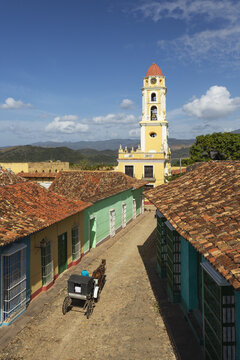 View of a horse-drawn carriage on a cobblestone street near the Convento de San Francisco de Asis, surrounded by colorful colonial buildings in Trinidad, Sancti Spiritus, Cuba.