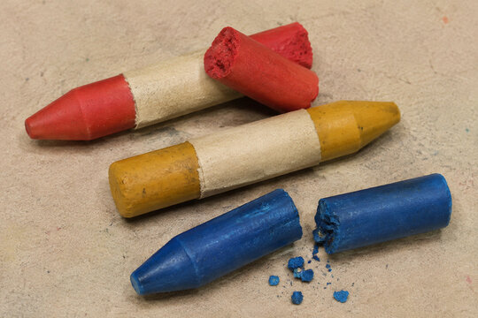 Broken red and blue wax crayons beside a yellow crayon