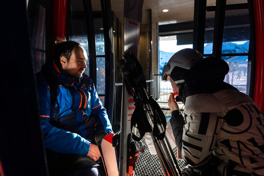 Scenic two skiers study trail map inside ski lift gondola at warm sunrise light at mountain alpine resort. Scenery group friends teamwork, planning, and excitement downhill winter sports adventure