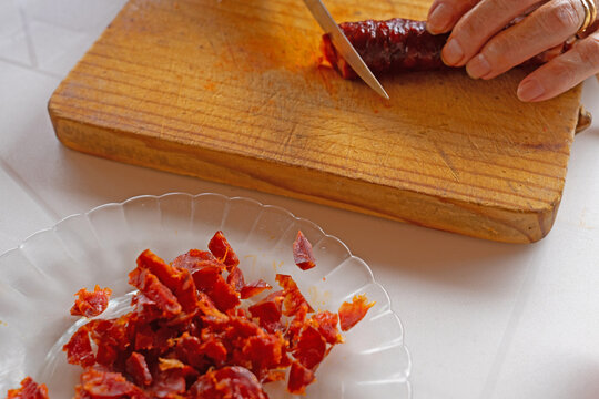 A hand cutting chorizo on a wooden board for tapas or recipe