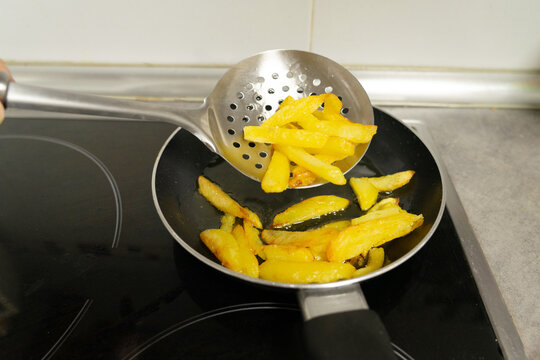 Chef lifting golden, crispy fries from the hot pan with a stainless steel slotted spoon