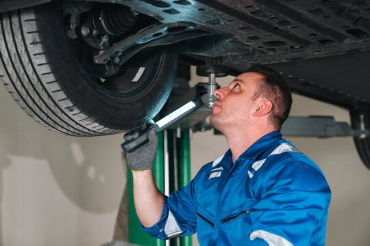 Electric vehicle battery car service Automotive mechanic inspecting vehicle undercarriage with flashlight during repair work