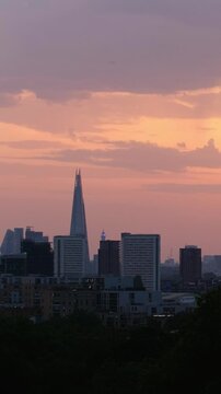 Vertical telephoto view of London's skyline featuring the BT Tower and The Shard beneath a soft pink and orange sky during golden hour.