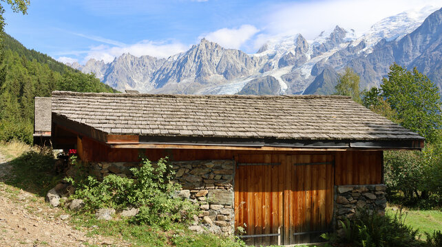 View of a traditional wooden barn with a stone base set against the backdrop of the melting glaciers at the Mont Blanc massif in Chamonix, Auvergne-Rhone-Alpes, France.