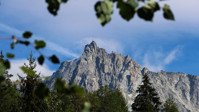 View of the rugged peaks of the Mont Blanc massif with rocky textures and sparse snow under a clear blue sky, framed by pine branches in Chamonix, Auvergne-Rhone-Alpes, France.