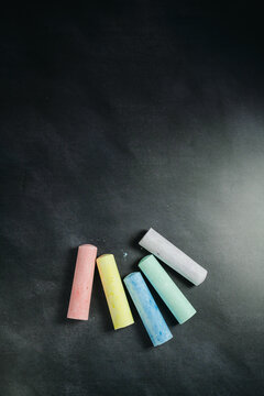 Colorful chalk sticks on blackboard surface, education mockup background