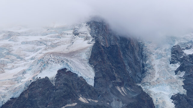 View of the melting glaciers and rugged rocky slopes of the Mont Blanc massif partially obscured by clouds in Chamonix, Auvergne-Rhone-Alpes, France.