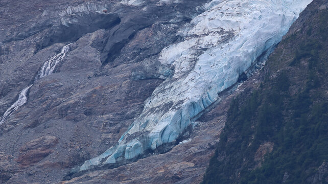 View of melting glaciers at the Mont Blanc massif with blue ice, rocky terrain, and cascading meltwater streams in Chamonix, Auvergne-Rhone-Alpes, France.